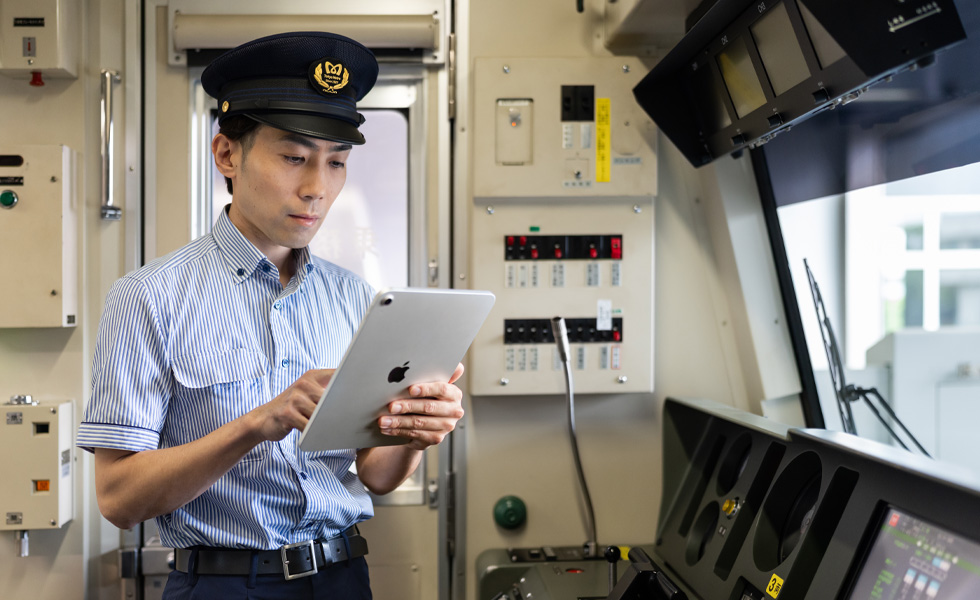En tunnelbaneförare använder en iPad medan han står i den upplysta förarhytten på tåget han kör.