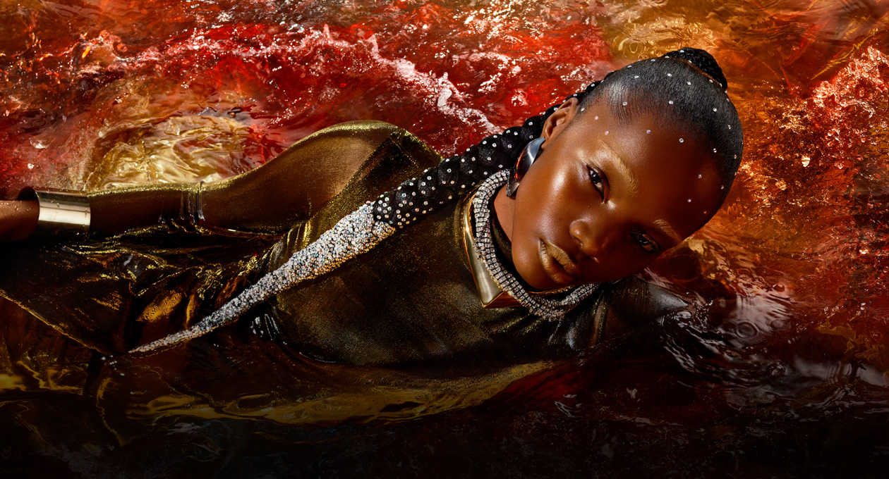 Image d’une personne vêtue d’une robe or métallique allongée sur le côté dans une piscine d’eau rouge, illustrant la luminosité, le contraste et la gamme de couleurs étendue du Studio Display XDR
